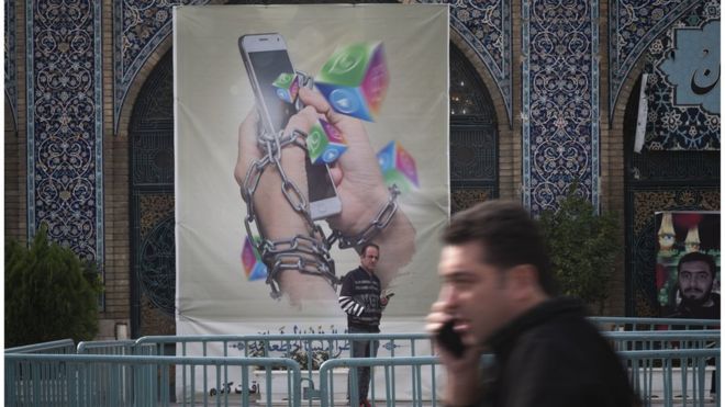 An Iranian man holding his smartphone looks on while standing under an anti-social networking banner in Tehran Grand Bazaar on 3 December 2022.
