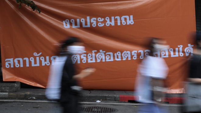 ผู้ชุมนุมเดินผ่านป้ายเรียกร้องให้ตรวจสอบงบประมาณเกี่ยวกับสถาบันกษัตริย์