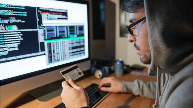 Un hombre sostiene una tarjeta de crédito frente a un monitor.