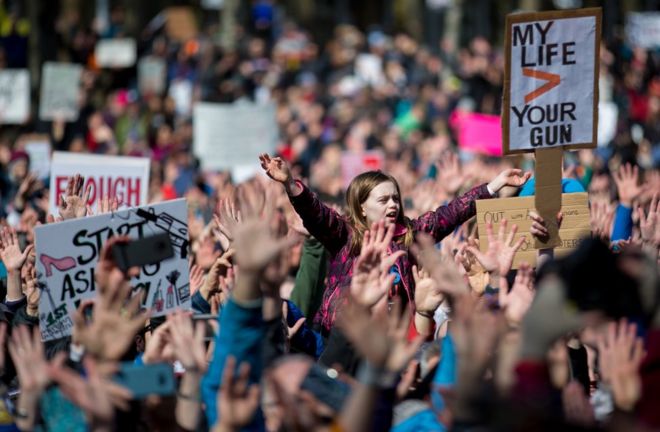 24 марта 2018 года в Сиэтле молодая девушка поднимает руки вместе с сотнями других.