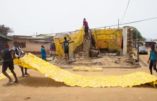 Люди расстилают желтый гобелен, созданный художником Сержем Аттуквеем Клотти на дороге в Ла - Аккра, Гана