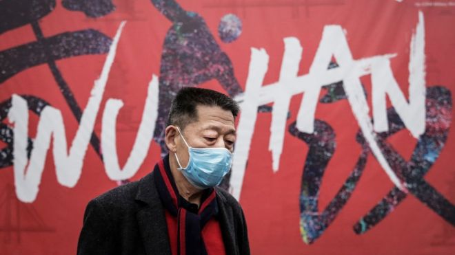 Un hombre frente a un mural que dice Wuhan