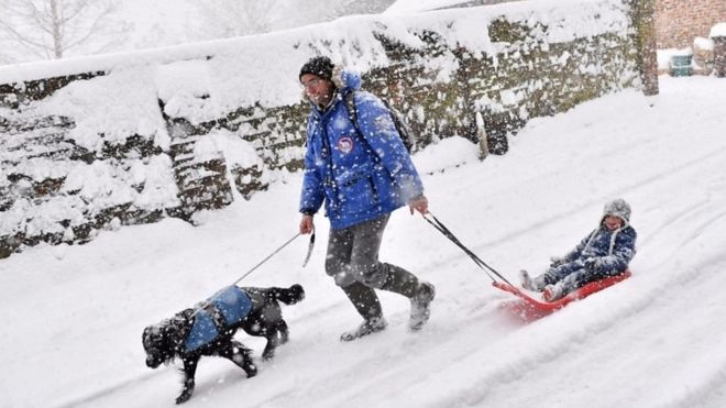 A man walks with his dog and pulls his child along in a sledge in southeast England
