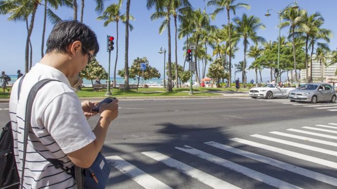 Мужчина смотрит на свой мобильный телефон перед тем, как перейти улицу в Гонолулу