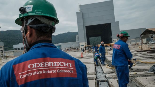 рабочий в каске с логотипом Odebrecht на спине униформы