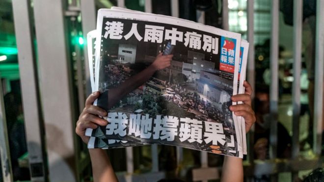 An employee holds up the latest copies of the Apple Daily newspaper