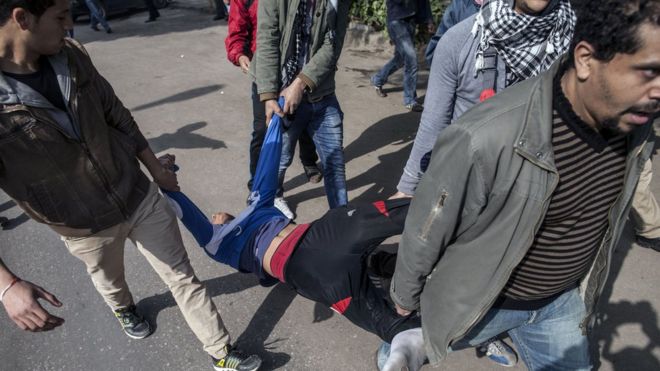 Египетские антиправительственные демонстранты несут человека, раненного резиновой пулей, выпущенной полицией во время столкновений в Каире 25 января 2014 года