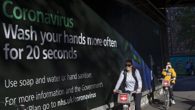 Люди проезжают мимо правительственной рекламы коронавируса в Лондоне