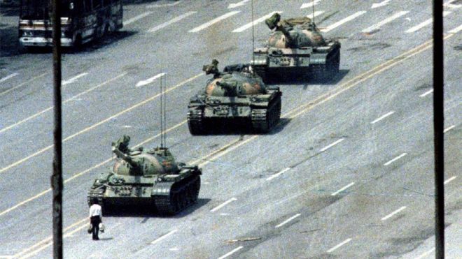 Знаменитый человек-танкист изображает одинокого человека с сумками, стоящего перед рядом танков