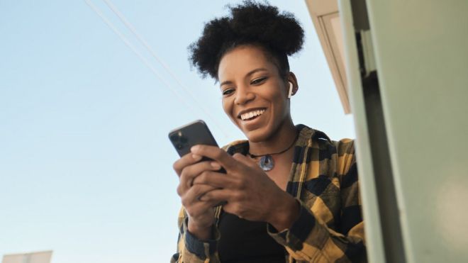 Una mujer sonríe mientras mira su celular.