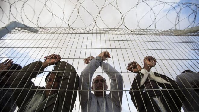 17 февраля 2014 года лица, ищущие убежища из Африки, которые незаконно въехали в Израиль через Египет, прислоняются к забору центра содержания под стражей Холот в южной части пустыни Негев в Израиле, когда они присоединяются к другим мигрантам, которые вышли на акцию протеста возле места содержания под стражей.