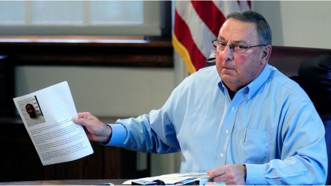 Maine Gov. Paul LePage holds up news release with a booking mug shot from a three-ring binder of news releases and articles about drug arrests during a meeting with reporters on Friday, Aug. 26, 2016,