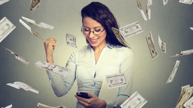 Mujer con teléfono móvil rodeada de billetes de dólares