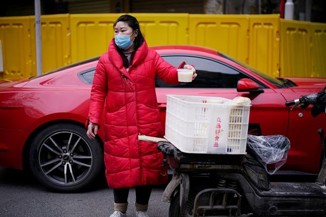 A vendor wearing a face mask sells soup on a street