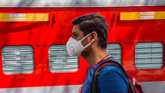 A man wearing a face mask walks past an Indian Railway train coach which is being set up for isolation