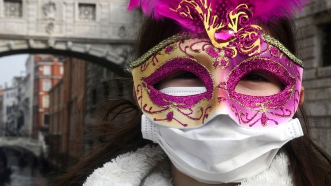 A person in a decorative mask and a face mask at the Venice Carnaval