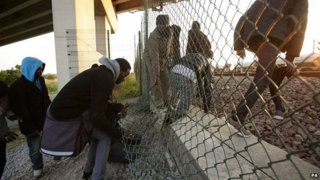 Мигранты поднимаются через забор к следам возле площадки Евротоннеля в Кокель в Кале, Франция.