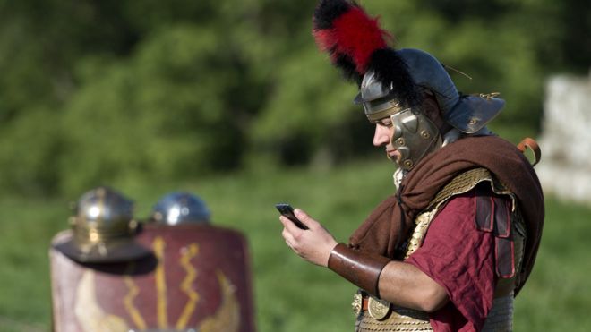 Человек в костюме римского солдата смотрит на мобильный телефон