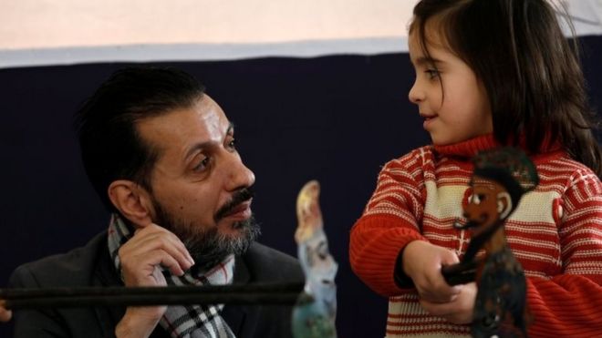 Шади аль-Халлак, кукловод, виден рядом с ребенком-инвалидом во время выступления в Дамаске, Сирия, 3 декабря 2018 года.