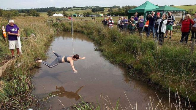 Crowds watches as a woman jumps, arms and legs spread, into the water