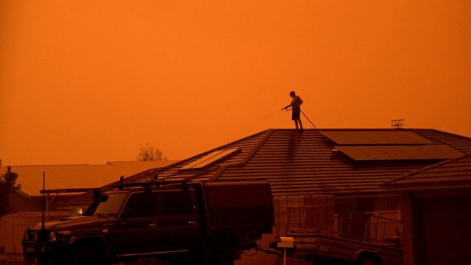 Um morador usa uma mangueira de jardim para molhar a casa enquanto ventos fortes espalham fumaça e cinzas do incêndio que atinge Nova Gales do Sul, na Austrália