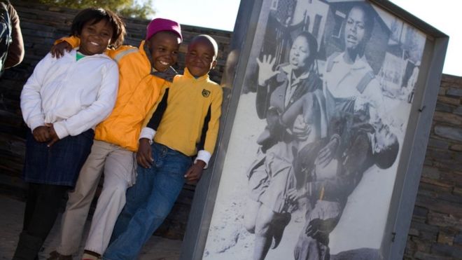 Южноафриканские дети позируют рядом со знаменитой фотографией 13-летнего Гектора Питерсона, которую несут студенты в музее Гектора Питерсона в Соуэто 16 июня 2010 года