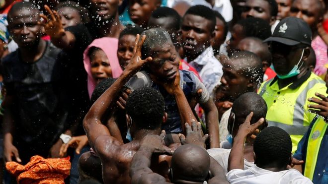 Люди разбрызгивают воду на ребенка, которого спасли на месте обрушившегося здания со школой в коммерческой столице Нигерии - Лагосе, Нигерия, 13 марта 2019 года
