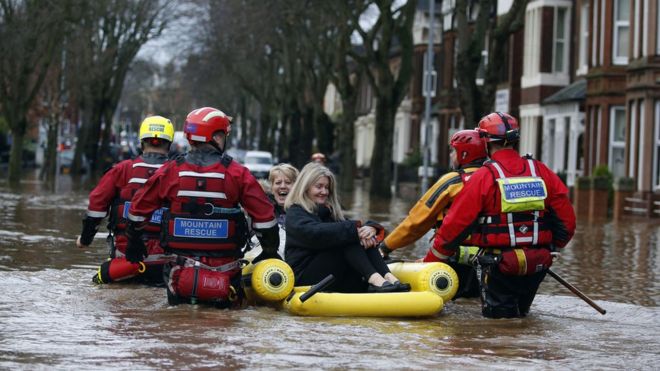 Аварийные работники используют надувной плот, чтобы спасти двух женщин от наводнения
