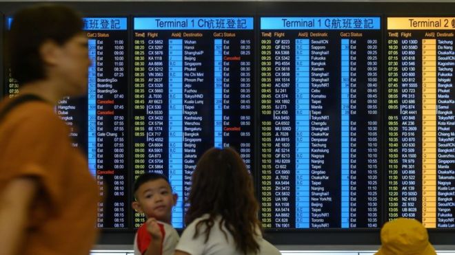 Passengers check the status of their flights on an electronic board at Hong Kong international airport on August 14, 2019.