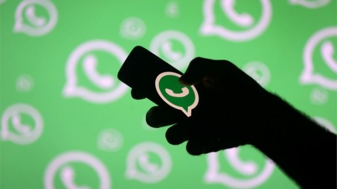 Человек с смартфоном перед логотипом WhatsApp, 4 июля 2018 года