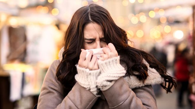 A woman blowing her nose on a tissue