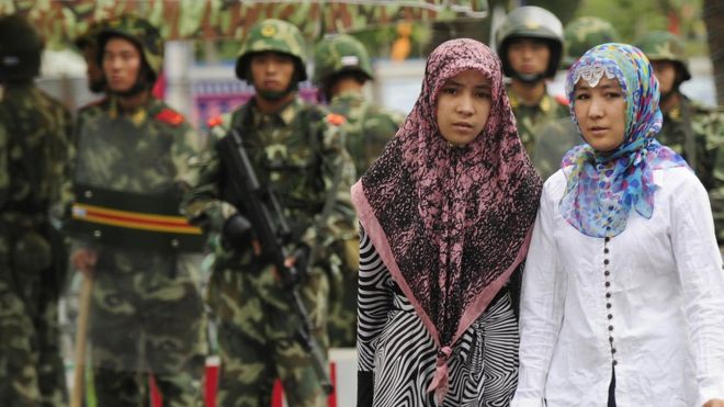Две уйгурские женщины передают китайских военизированных полицейских в Синьцзянском районе Китая