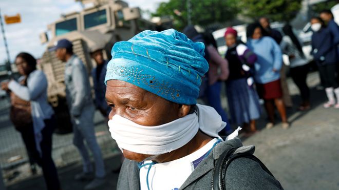 An elderly woman covers her face with a makeshift mask as people queue to collect social grants and shop during a 21 day nationwide lockdown aimed at limiting the spread of coronavirus disease (COVID-19) in Khayelitsha township near Cape Town