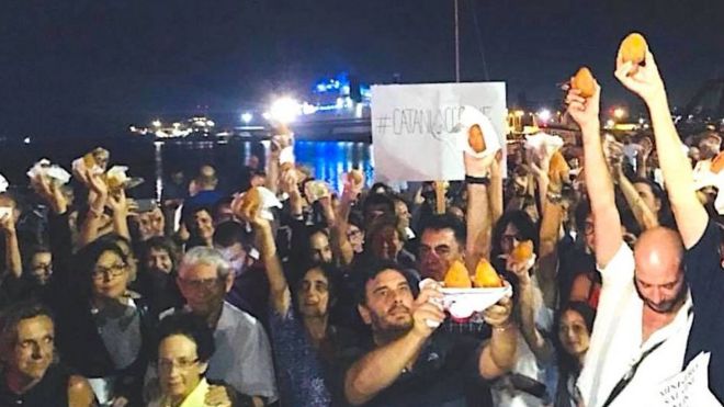 Протестующие размахивают аранчини в Катании, Сицилия, где на лодке около 200 спасенных мигрантов, которым было отказано в разрешении высадки