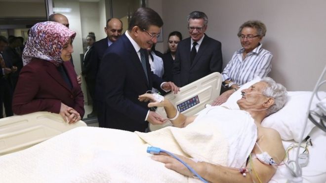 Премьер-министр Турции Ахмет Давутоглу, его жена Саре (слева) и министр внутренних дел Германии Томас де Мезьер (2-й справа) навестили жертву теракта во вторник в стамбульской больнице (13 января 2016 года)