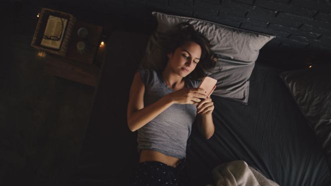 Mujer mirando el celular en la cama