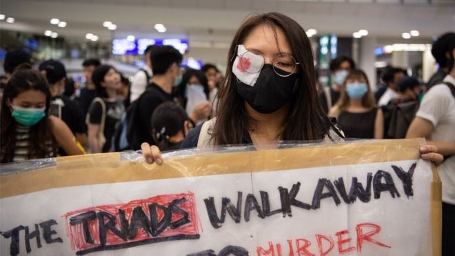 Женщина носит повязку на глазу в знак протеста против насилия со стороны полиции во время сидячей забастовки в международном аэропорту Гонконга Чек Лап Кок, Гонконг