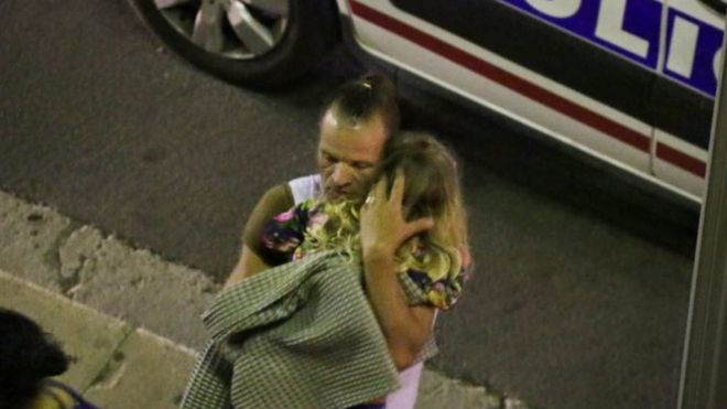 Мужчина держит ребенка после того, как грузовик пахал через гуляк Дня взятия Бастилии во французском курортном городе Ницца (15 июля 2016 года)
