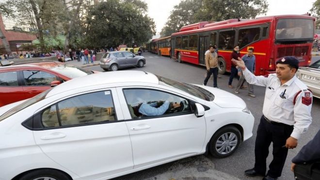 Индийский полицейский направляет движение на дороге до реализации схемы нечетного транспортного средства в Нью-Дели, Индия