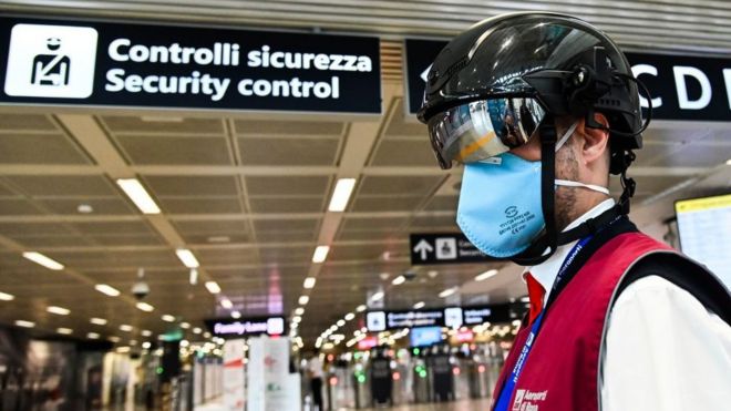 Image shows a Fiumicino airport employee wearing a "Smart-Helmet" portable thermoscanner to screen passengers and staff for COVID-19