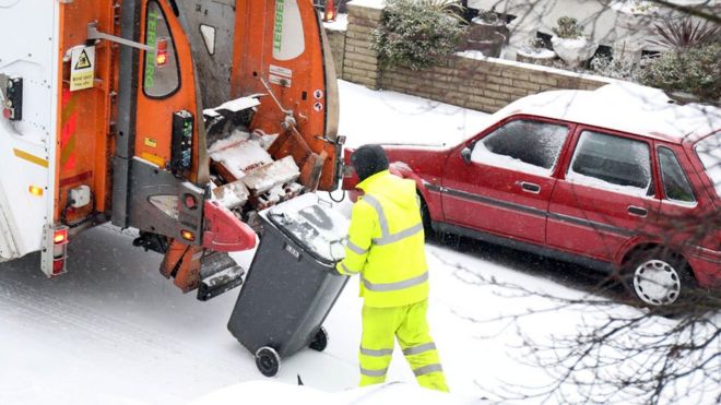 Бинман кладет мусорное ведро в грузовик на снегу