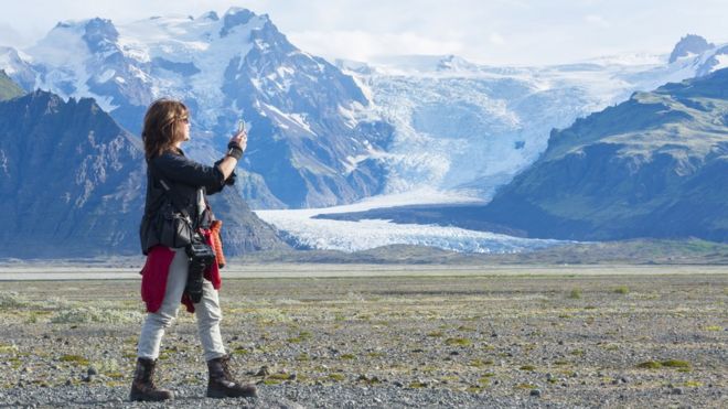 Mulher tira foto de paisagem com montanhas e neve na Islândia