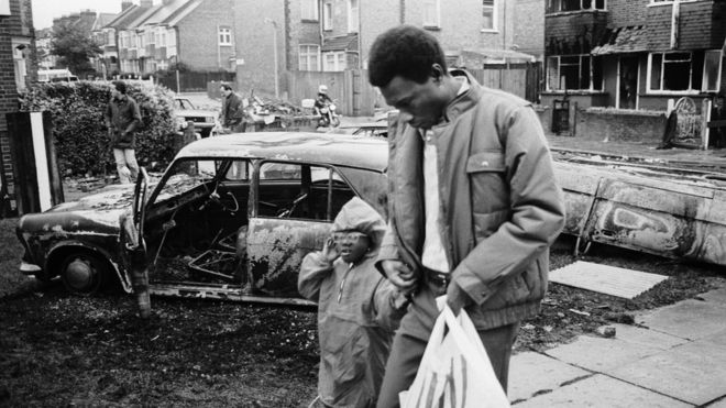 Мужчина и маленькая девочка на следующий день после беспорядков на Бродуотер-Фарм 6 октября 1985 года