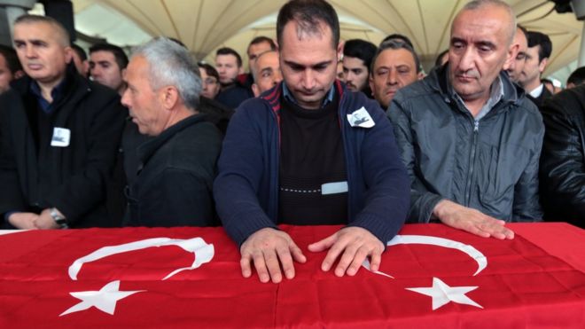Люди стоят у гроба, накинутого на турецкий флаг, для турецкого агента безопасности, убитого взрывом самоубийства