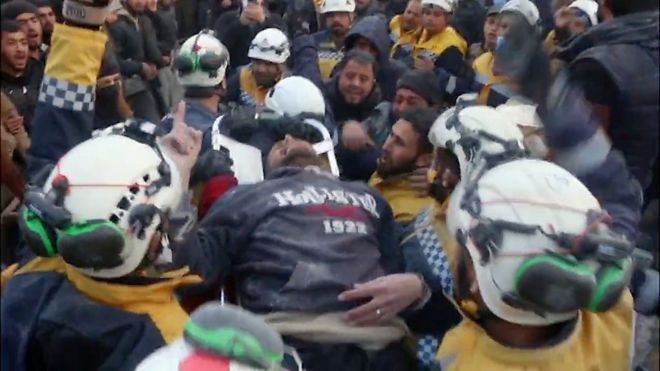 Man carried on stretcher surrounded by crowd