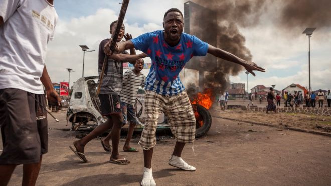 Демонстранты собираются перед горящей машиной во время митинга оппозиции в Киншасе 19 сентября 2016 года.