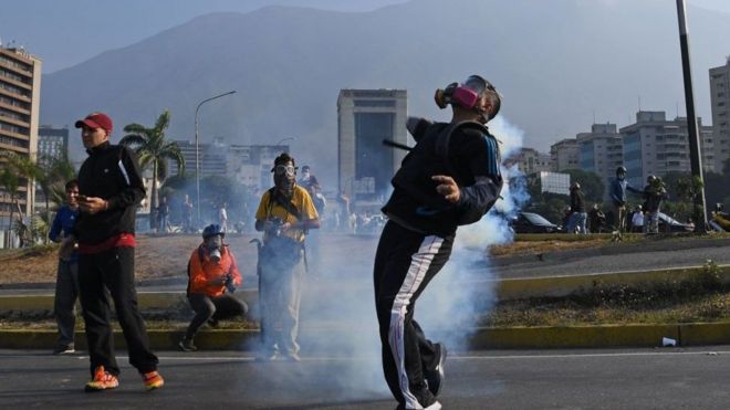 Un manifestante intenta lanzar una lata de gas lacrimógeno