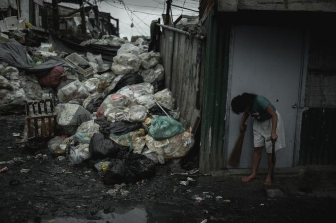 Женщина подметает перед своим домом в Хэппилленде свалку в Тондо, Манила