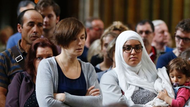 Muslim woman carries a child as people attend a Mass in the Rouen Cathedral