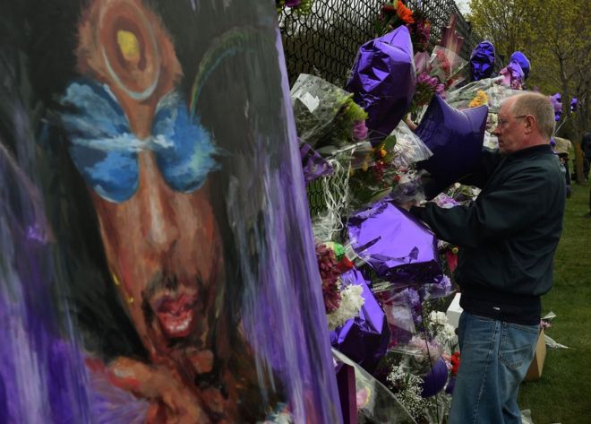 Поклонники принца прикрепляют цветы к мемориальной стене, когда он отдает дань уважения у жилого парка Пейсли в Миннеаполисе, штат Миннесота, 22 апреля